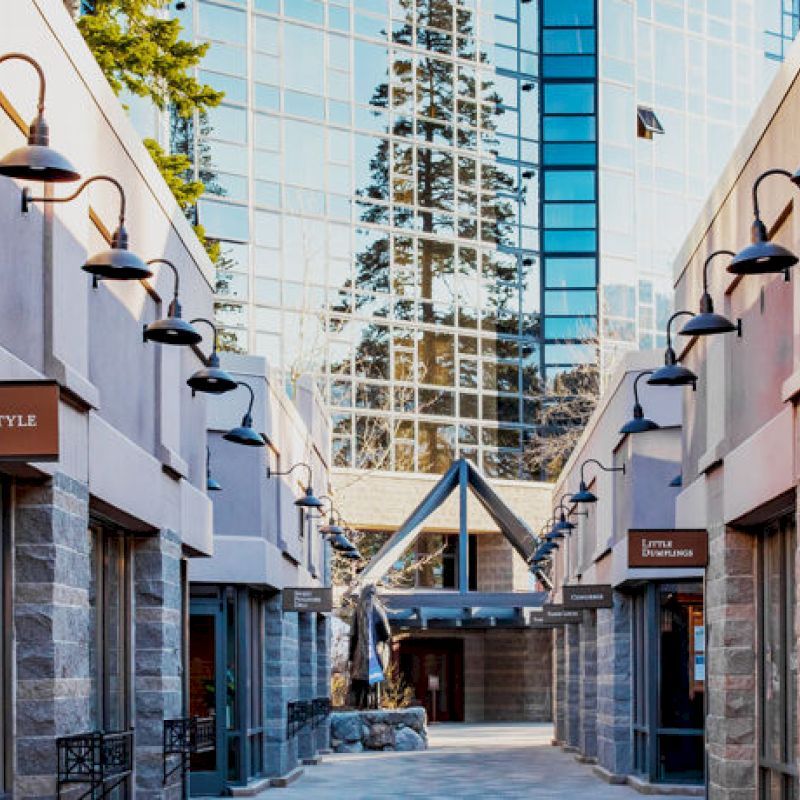 A narrow shopping alley with various stores, such as Tahoe Style and Double Diamond Jewelry, and a glass building in the background.