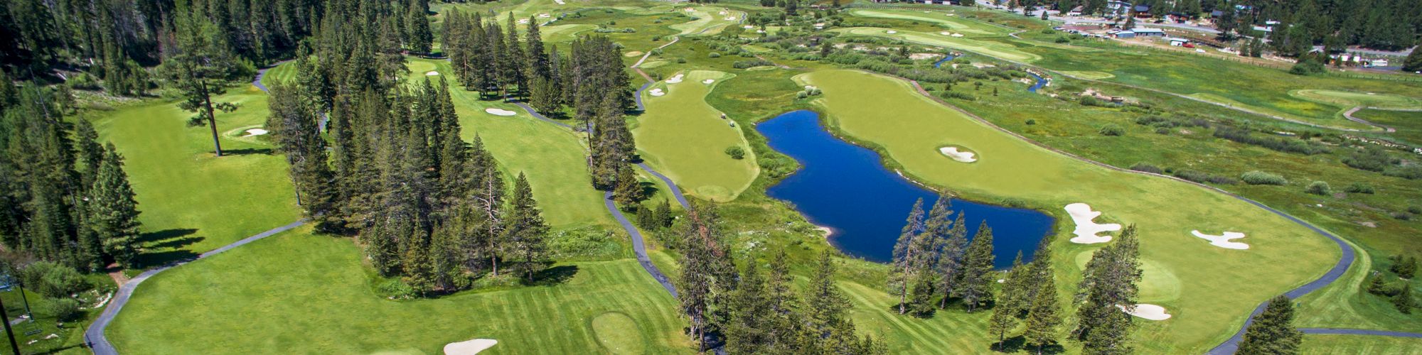 This image shows an aerial view of a golf course surrounded by trees and mountains, with a pond in the center and several sand bunkers.