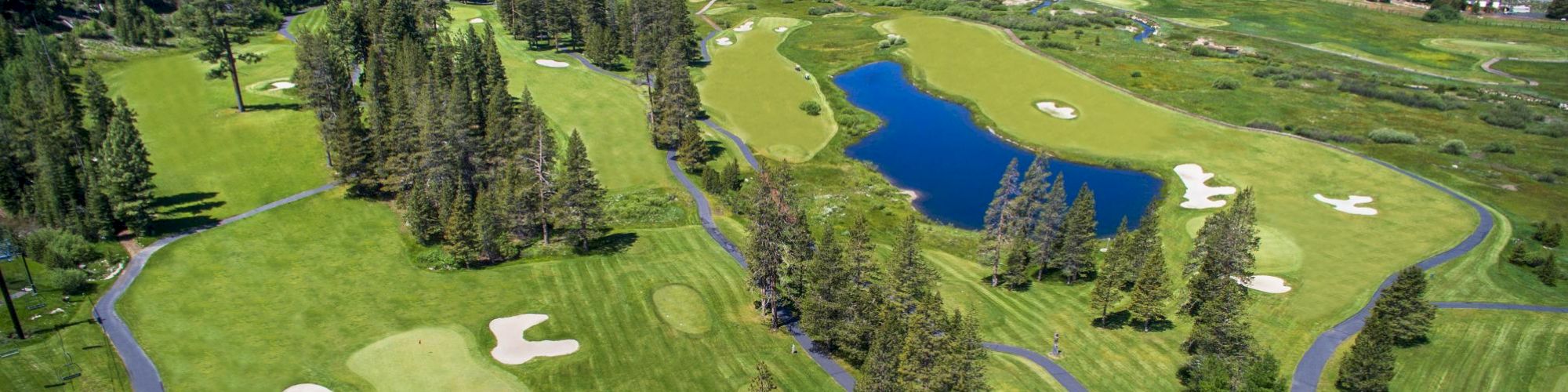 This image shows an aerial view of a scenic golf course surrounded by trees and mountains, with a lake in the middle, set in a beautiful valley.