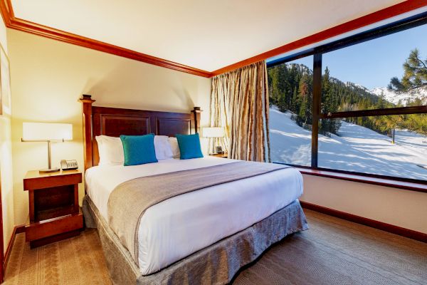 A cozy hotel room with a large bed, two side tables with lamps, and a window offering a snowy mountain view ending the sentence.