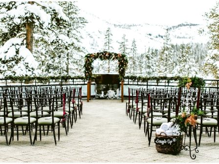 A snow-covered outdoor wedding setup with rows of chairs, an arched altar with floral decorations, and a scenic mountain backdrop, ending the sentence.