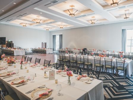 A decorated banquet room with long tables, white tablecloths, chairs, and flower arrangements, ready for an event or reception.