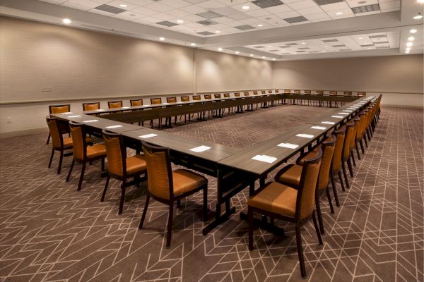 The image shows a U-shaped conference room setup with rows of chairs and tables aligned, with notepads placed on the tables, and a carpeted floor.