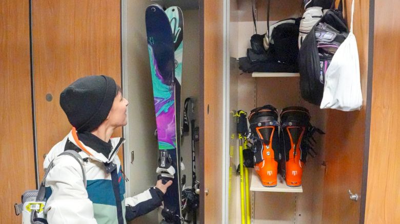A person is organizing ski gear in a locker that includes skis, ski poles, boots, helmets, gloves, and other skiing accessories.