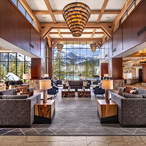 A spacious, modern hotel lobby with large windows showcasing a mountain view, comfortable seating areas, and elegant chandeliers.