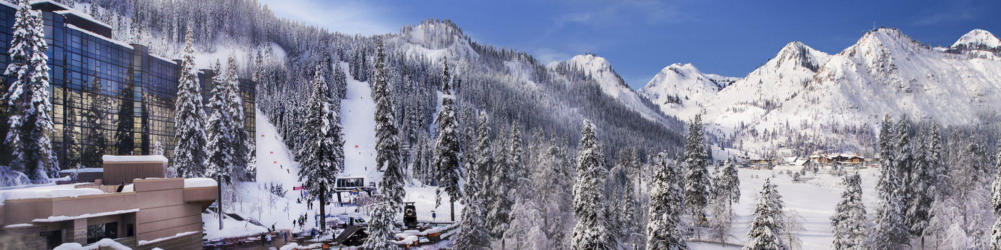 A snowy mountain resort with ski slopes, buildings, pine trees, and a partially frozen pond, set against a backdrop of snow-covered peaks.