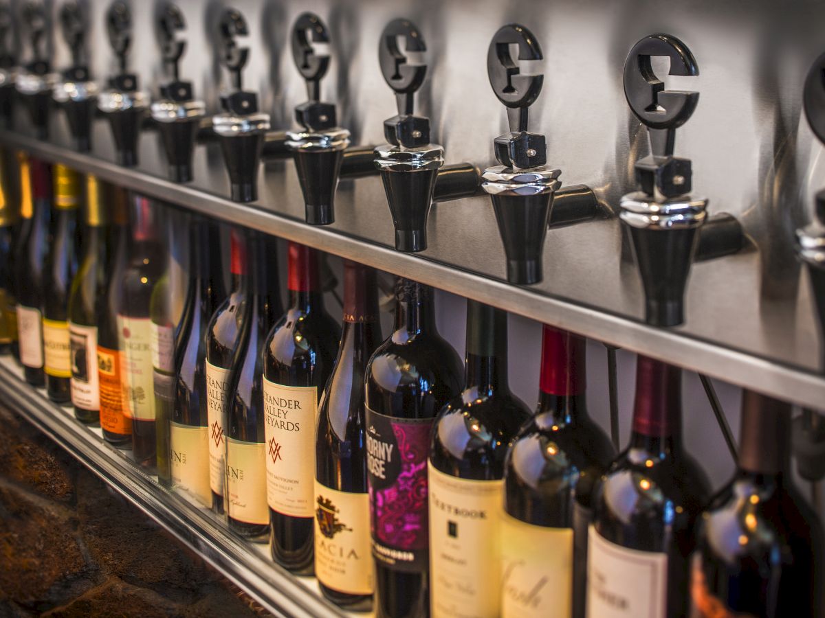 The image shows a row of wine bottles placed under wine dispensers. The set-up appears to be designed for a wine tasting or bar setting.