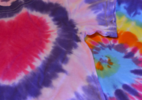 The image shows two colorful tie-dye shirts with vibrant patterns, including a heart-shaped design and a multicolored circular design.